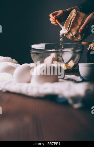 Les mains de femmes de verser la farine dans un bol avec du beurre à côté d'ingrédients pour gâteau. Vertical image processus de préparation de la pâte à tarte. Banque D'Images