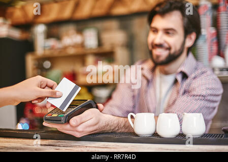 Smiling dark-haired bartender sert femme debout près de comptoir de café, de payer pour l'ordre Banque D'Images