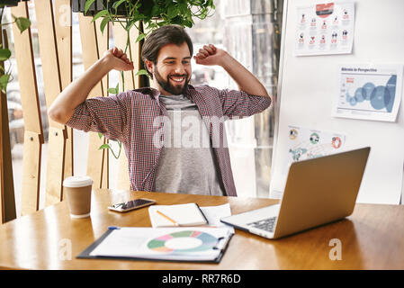 Young Woman in casual wear étend ses bras et du corps pour se détendre tout en travaillant au bureau avec ordinateur portable. Une tasse de café, Smartphone, ordinateur portable sur une table en bois. Pour prévenir le syndrome d'office au repos Banque D'Images