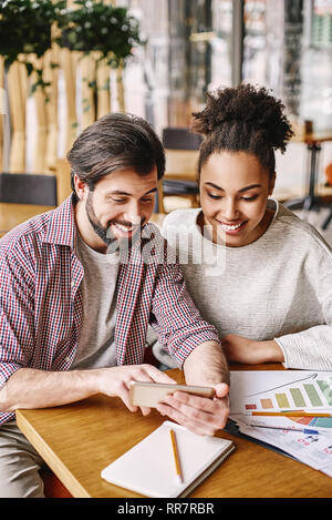 Couple de jeunes designers travaillant au bureau moderne, deux collègues discuter projet amusant, peu d'affaires de l'équipe de sourire et à la ensemble au téléphone. Documents de travail et les crayons sont sur le bureau. Style décontracté. Concept de la réussite Banque D'Images