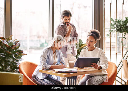 Groupe de jeunes collègues discuter des idées les uns avec les autres dans un bureau moderne. Les gens d'affaires à l'aide d'un ordinateur portable. Deux jeunes femme et brun sont concentrés en travaillant sur un nouveau projet. Lieu de travail confortable, horizontale Banque D'Images