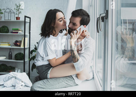 Beautiful woman hugging man talking on smartphone à la maison Banque D'Images