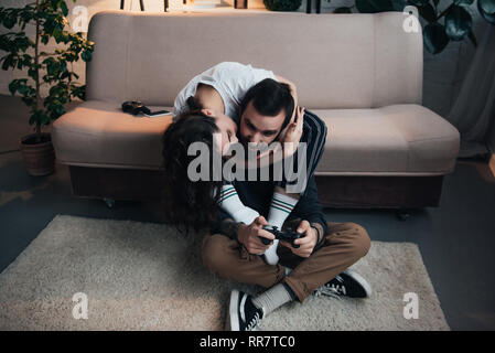 Embrasser femme homme jouant avec la manette de jeu vidéo dans la salle de séjour Banque D'Images