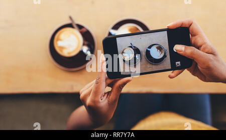 POV shot of woman photographing tasses à café sur la table de café avec son téléphone intelligent. Femme faisant la photographie culinaire avec son téléphone portable pour son enseignement social Banque D'Images