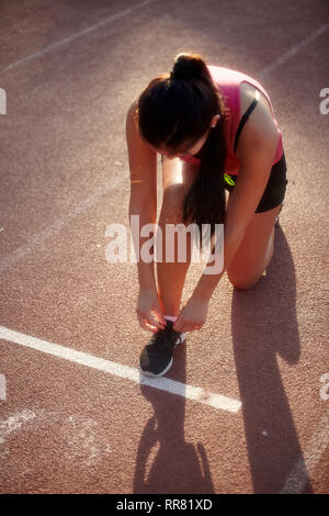 Une jeune femme, lier ses lacets sur les pistes de course de sport. coup de ci-dessus. Banque D'Images