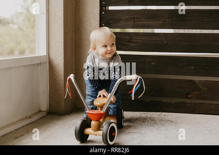 Adorable précieux petit Blond bébé Bébé garçon enfant jouer dehors sur jouet en bois Location Scooter Smiling at the Camera Mobile et d'avoir du plaisir Banque D'Images