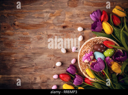 Oeufs de Pâques dans un panier avec des tulipes sur fond de bois vieux Banque D'Images