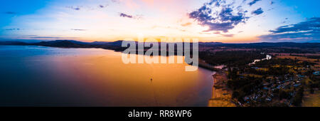 Seul bateau naviguant à travers le pittoresque lac au coucher du soleil orange vif - panorama aérien Banque D'Images
