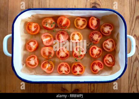 La préparation des tomates pour le séchage au soleil ou grillage. Couper les tomates, avec du thym et d'huile d'olive, sur le papier sulfurisé et en émail bleu et blanc à l'étain. Haut Banque D'Images