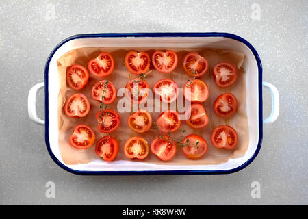 La préparation des tomates pour le séchage au soleil ou grillage. Couper les tomates, avec du thym et d'huile d'olive, sur le papier sulfurisé dans un émail morts sur le béton Banque D'Images