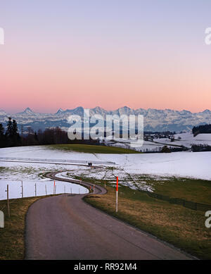 Chemin qui mène à travers les collines d'hiver sur la montagne Gurten colorés avec ciel en soirée et célèbre Jungfrau (Eiger, Mönch et Jungfrau) dans e Banque D'Images