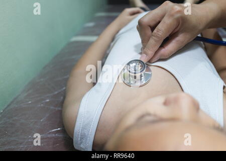 Le médecin examinant la fille asiatique et écouter heartbeat avec stéthoscope dans l'hôpital. Banque D'Images