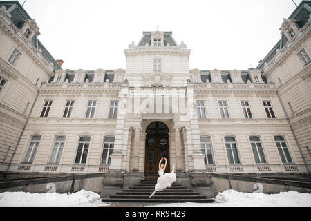 Belle robe blanche ballerine en sautant à côté du bâtiment sur la neige fond. Banque D'Images