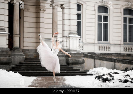 Belle danse ballerine en robe blanche à côté du bâtiment sur la neige fond. Ballet Arabesque poser. Banque D'Images