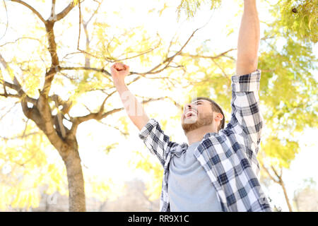 Guy excité Célébrons les succès raising arms dans un parc avec des arbres en arrière-plan Banque D'Images