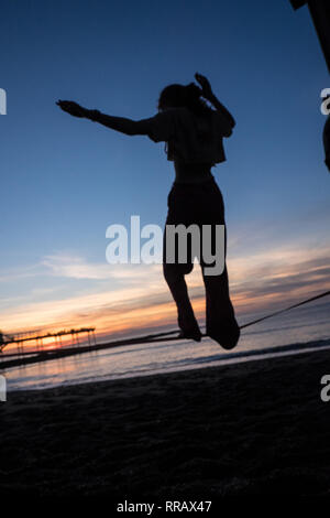 Météo France : février le plus chaud jamais enregistré au Royaume-Uni à Ceredigion,avec plus de 20 degrés de température de jour.ici les étudiants universitaires sur une slack line et Royal Pier silhouette.Aberystwth,soleil,Cerdigion,Royaume-Uni Pays de Galles Banque D'Images