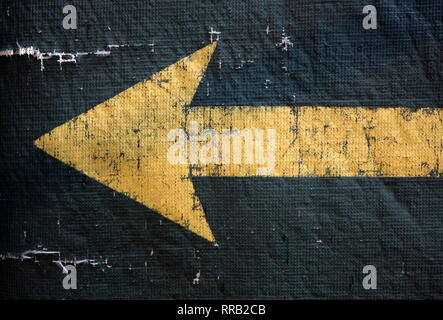 Une flèche jaune pointant vers la gauche sur une bâche vert usé Banque D'Images