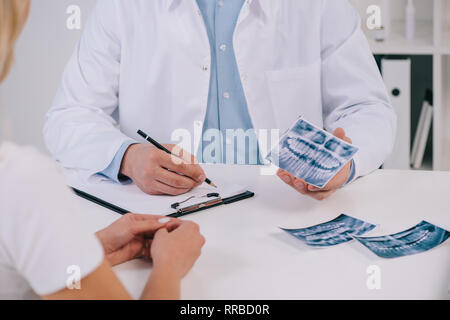 Portrait de l'orthodontiste dents holding x-ray et l'écriture de diagnostic lors de consultations avec female patient in clinic Banque D'Images