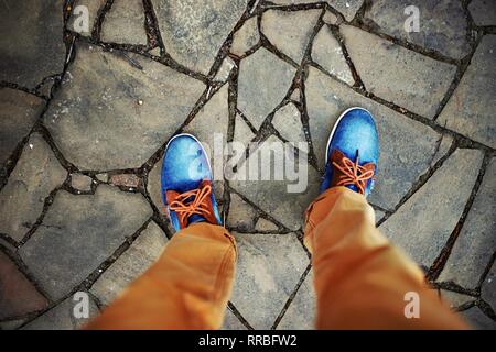 Les pieds des hommes en jeans denim sneakers et Rusty sont debout sur un plancher de carreaux de pierre sauvage Banque D'Images