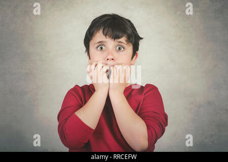 Scary kid qui mord ses ongles contre l'arrière-plan gris Banque D'Images