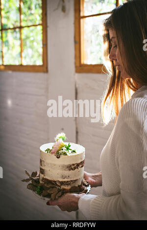 Vue latérale du petit plaisir dame holding dish avec de savoureux gâteau décoré par chrysanthemum bud et des feuilles sèches dans la chambre Banque D'Images