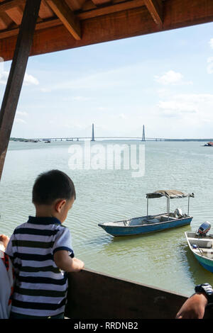 Voir l'avant-plan flou des enfants de regarder le bateau amarré par la jetée en bois avec johor River Bridge en arrière-plan. Vue depuis une jetée en bois Banque D'Images