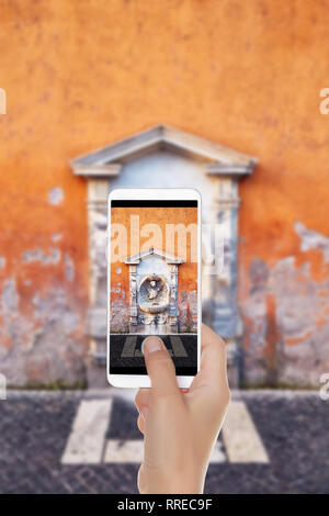 Un homme fait une photo de la petite fontaine d'eau potable avec la sculpture et la décoration en pierre en mauvais état mur peint, Rome sur un téléphone mobile Banque D'Images