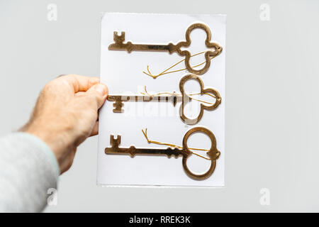 Man holding against white background d'un jeu de trois clés d'or antique vintage - vertical holding Banque D'Images