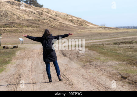 Stock Photo de portrait femme en manteau noir bras levés sur la route vide vers le coucher du soleil l'horizontale Banque D'Images