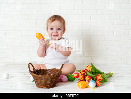 Mignon bébé garçon assis avec des oeufs de Pâques et des tulipes contre fond blanc Banque D'Images