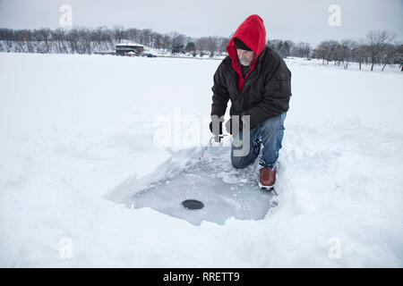 Un homme d'âge moyen de la pêche sur glace sur un lac dans le Minnesota enneigé pendant l'hiver Banque D'Images