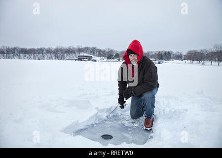 A smiling middle aged man Ice fishing on a snowy Lake dans le Minnesota pendant l'hiver Banque D'Images