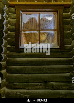 Fenêtre dans une cabane en bois avec la neige et les lumières à l'intérieur Banque D'Images