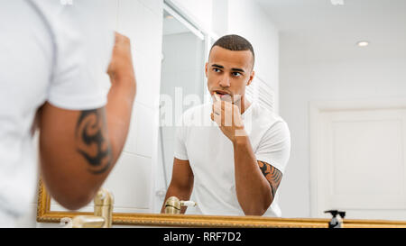 L'homme à la recherche de miroir et se brosser les dents dans la salle de bains Banque D'Images