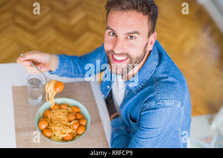 Bel homme de manger des pâtes avec des boulettes de viande et de la sauce tomate à la maison tout en souriant à l'appareil photo Banque D'Images