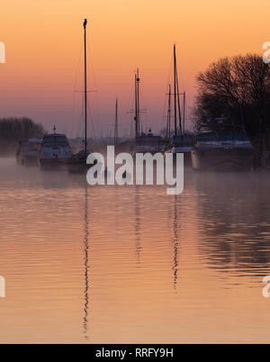 Wareham, Dorset, UK. 26 février 2019. Météo France : Le ciel s'allume avec des teintes orange et rose comme la brume se lève au-dessus de la rivière Frome sur un froid matin de février. Une scène paisible que la voile bateaux amarrés le long de la rivière se reflètent dans l'eau calme sur le début de ce qui est défini pour être une autre journée ensoleillée glorieusement. Credit : Celia McMahon/Alamy Live News Banque D'Images