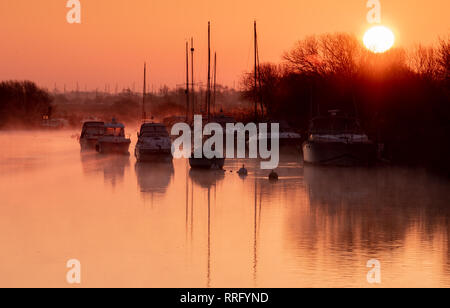 Wareham, Dorset, UK. 26 février 2019. Météo France : Le ciel s'allume avec des teintes orange et rose comme la brume se lève au-dessus de la rivière Frome sur un froid matin de février. Une scène paisible que la voile bateaux amarrés le long de la rivière se reflètent dans l'eau calme sur le début de ce qui est défini pour être une autre journée ensoleillée glorieusement. Credit : Celia McMahon/Alamy Live News Banque D'Images