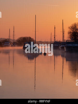 Wareham, Dorset, UK. 26 février 2019. Météo France : Le ciel s'allume avec des teintes orange et rose comme la brume se lève au-dessus de la rivière Frome sur un froid matin de février. Une scène paisible que la voile bateaux amarrés le long de la rivière se reflètent dans l'eau calme sur le début de ce qui est défini pour être une autre journée ensoleillée glorieusement. Credit : Celia McMahon/Alamy Live News Banque D'Images