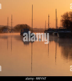 Wareham, Dorset, UK. 26 février 2019. Météo France : Le ciel s'allume avec des teintes orange et rose comme la brume se lève au-dessus de la rivière Frome sur un froid matin de février. Une scène paisible que la voile bateaux amarrés le long de la rivière se reflètent dans l'eau calme sur le début de ce qui est défini pour être une autre journée ensoleillée glorieusement. Credit : Celia McMahon/Alamy Live News Banque D'Images