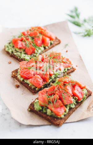 Vue rapprochée de trois sandwiches avec le pain de seigle, d'avocat et saumon fumé, sur une table de cuisine blanche. Banque D'Images