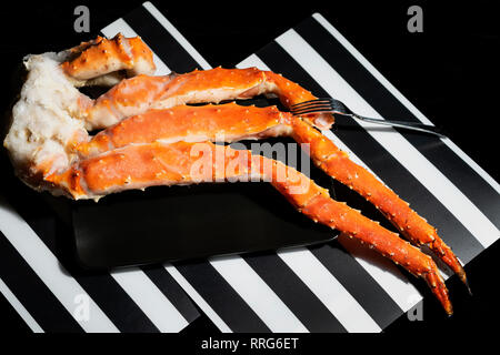 Les pattes de crabe et la fourchette dans la plaque noire sur fond rayé noir et blanc Banque D'Images