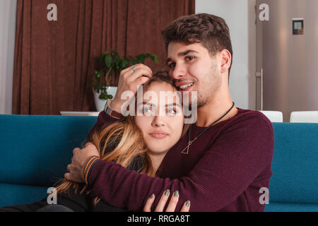 Heureux couple, man hugging sa femme alors qu'elle est pensée et à côté assis sur un canapé à la maison. Regarder la télévision dans le salon. Banque D'Images