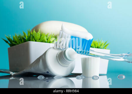 Nouvelle brosse à dents avec du dentifrice close-up dans la salle de bains sur un miroir table avec gouttes d'eau sur un fond bleu dans la lumière du soleil Banque D'Images