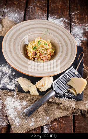 Les pâtes à la Carbonara de Parmesan sur une plaque blanche. Les repas au restaurant à la table en bois, à côté les ingrédients pour la cuisson Banque D'Images