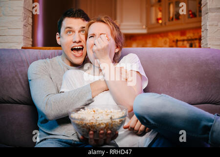 Jeune couple eating popcorn et regarder un film à la maison sur le canapé, de peur. Banque D'Images