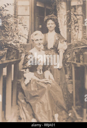 Carte postale photographique Vintage Edwardian habillés de deux femmes dans leur véranda ou jardin. De nombreuses plantes en pot sur l'affichage. Banque D'Images