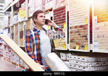 L'homme avec le smartphone choisit et achète des biens dans un supermarché de la construction Banque D'Images