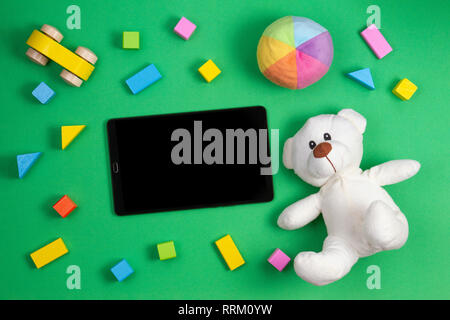 Jouets bébé enfant arrière-plan. Ours en peluche, les cubes colorés blocs, petite voiture et ordinateur tablette sur fond vert Banque D'Images