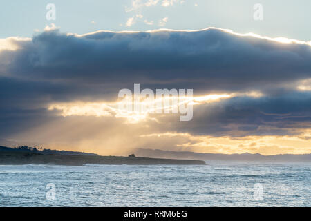 Nuages part lors d'un lever de soleil sur la côte de Californie. Créer de beaux rayons de lumière à travers l'ocean spray près de Cambria. Banque D'Images