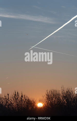 Lever du soleil. Avion de ligne à réaction grimpant depuis l'aéroport de Londres Heathrow au Royaume-Uni, avec des traînées aériennes traversant le ciel de l'aube. Départ du vol aérien Banque D'Images